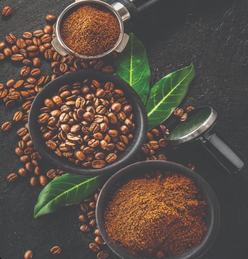 Granos de café artesanal, café molido y hojas verdes sobre una superficie oscura